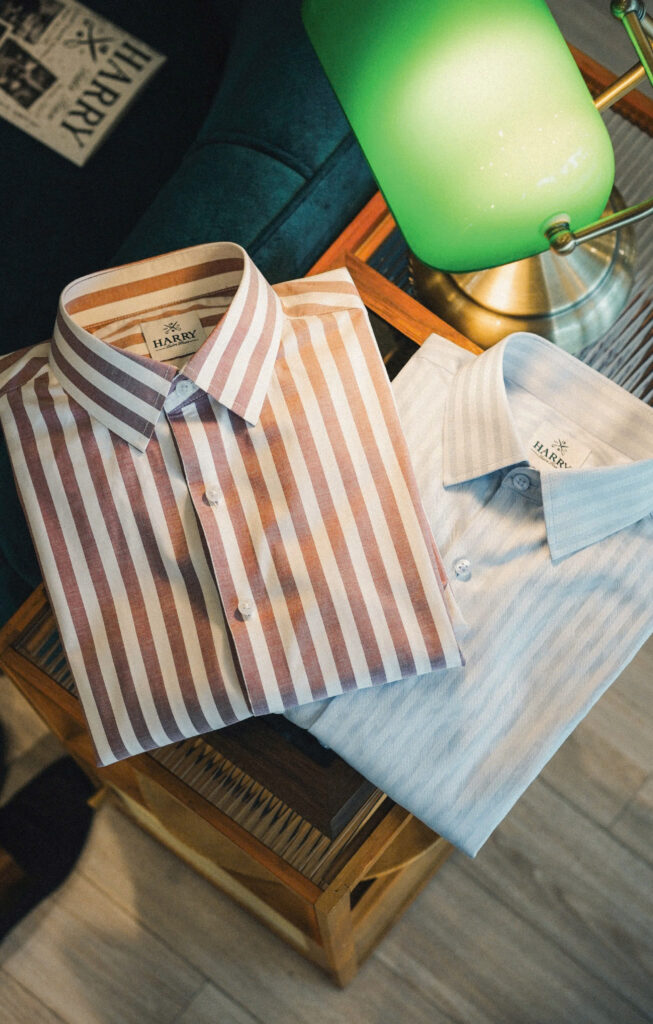 Two bespoke dress shirts neatly displayed on a wooden chair, showcasing fine tailoring and premium fabric design.