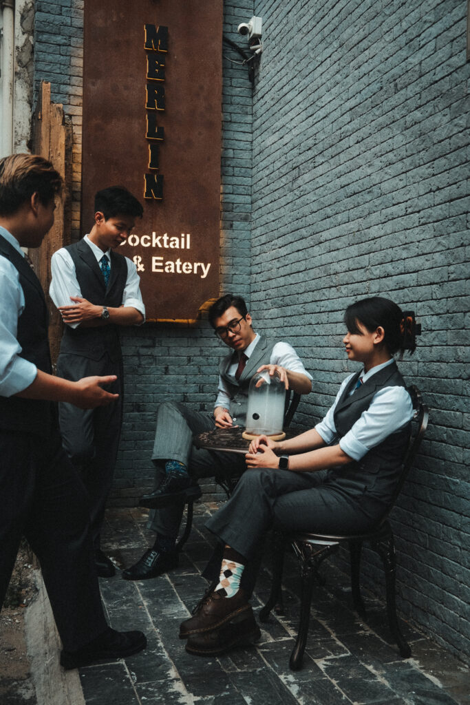 Staff in matching bespoke uniforms outside Merlin Cocktail & Eatery in Ho Chi Minh City, wearing tailored vests, trousers, and dress shirts – a showcase of bespoke uniform tailoring.
